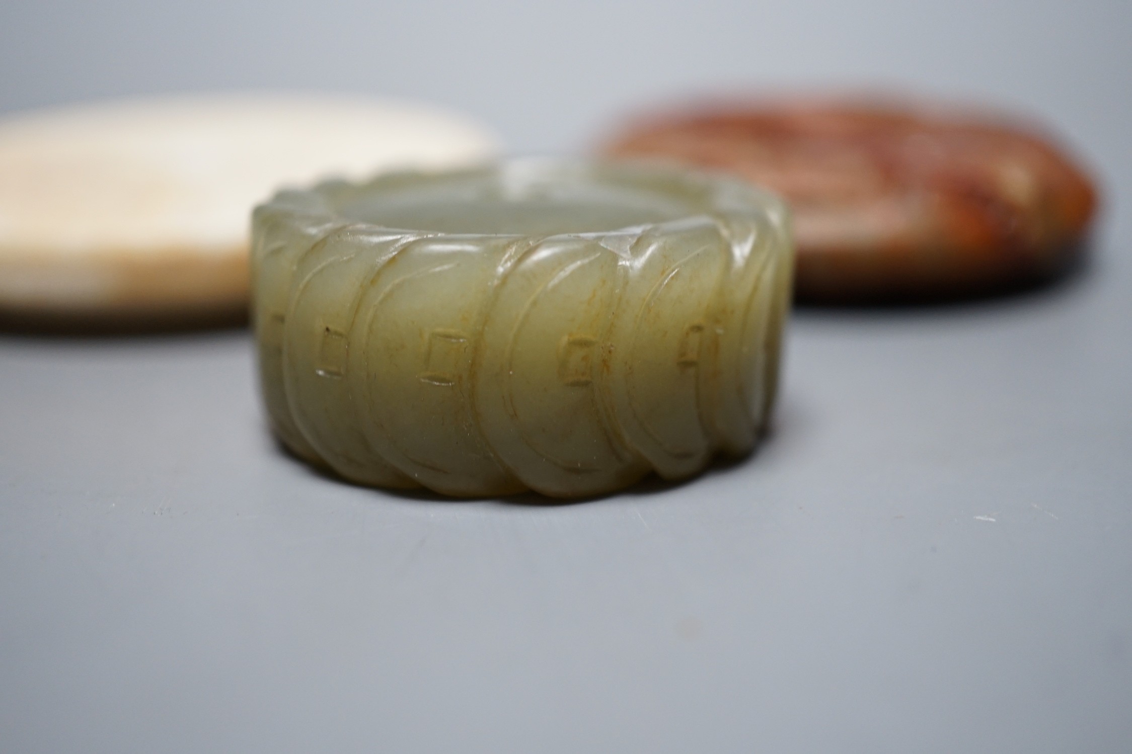 A Chinese green jade 'cash' pendant, a russet jade bi-disc and a burnt jade circular plaque